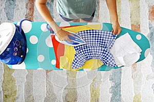 Aerial view of woman ironing kidÃ¢â¬â¢s clothes with steam on ironing board